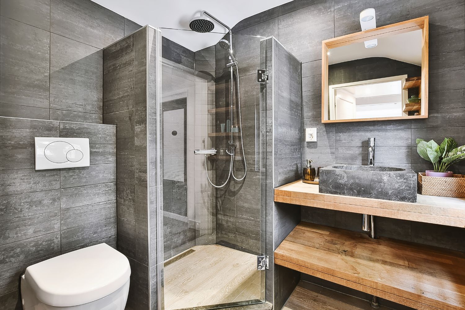 A completed bathroom renovation in Sydney with dark grey feature tiles, a frameless glass shower, wall-hung toilet and timber floating vanity with stone basin, designed and installed by 10X Joinery.