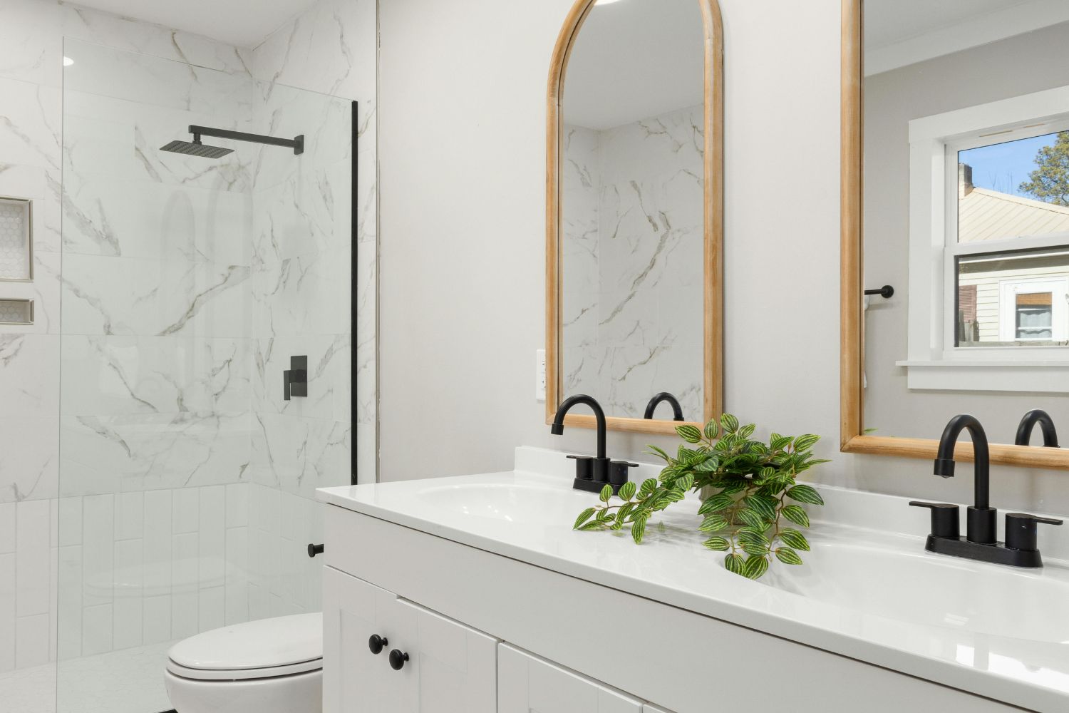 A white double vanity with black tapware, arched timber-framed mirrors and marble-look shower tiles, finished with durable wet-area materials by 10X Joinery, Sydney.