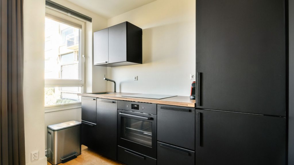 A compact black handleless kitchen with a timber benchtop and integrated fridge in a Bankstown apartment by 10X Joinery.