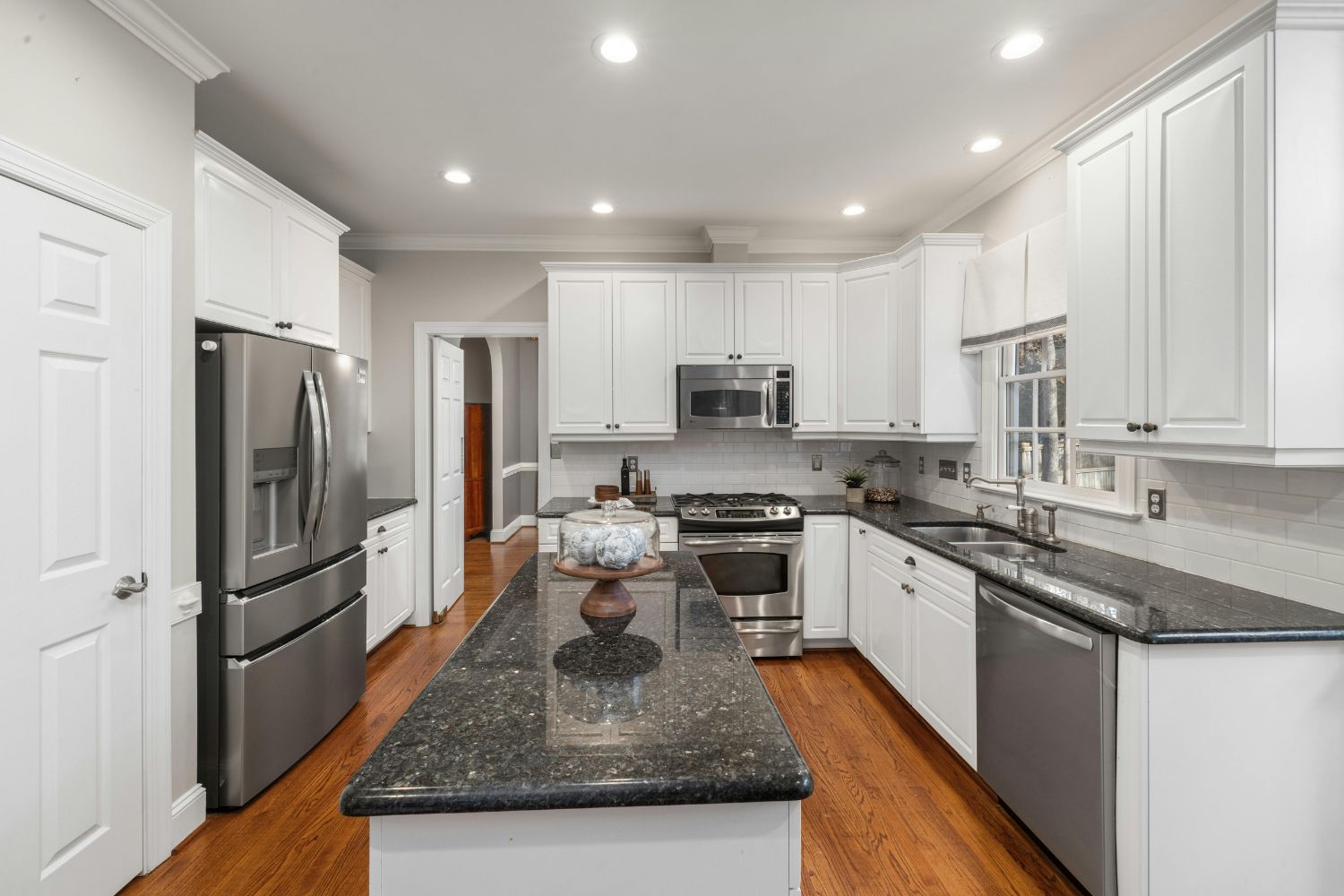 A kitchen renovation in Bankstown with white raised-panel cabinetry, a dark granite island and benchtops, stainless appliances and timber floors, designed and built by 10X Joinery.