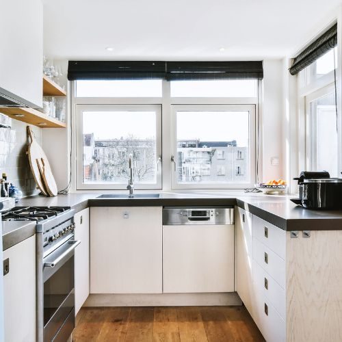 A compact white apartment kitchen near Bankstown town centre with tall cabinetry, a dark benchtop and timber floors by 10X Joinery.
