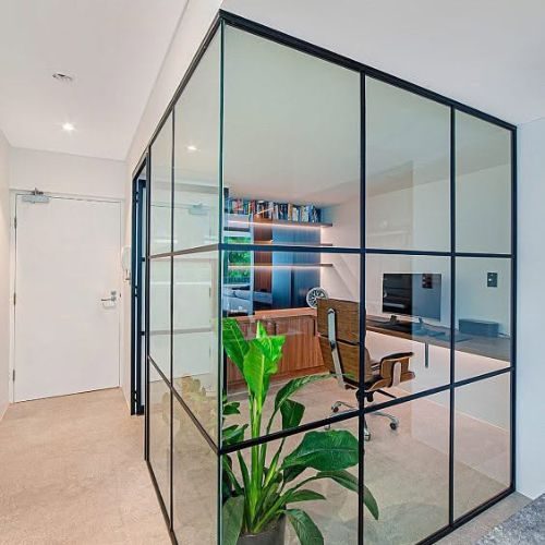 Steel-framed glass partition enclosing a home office with built-in shelving