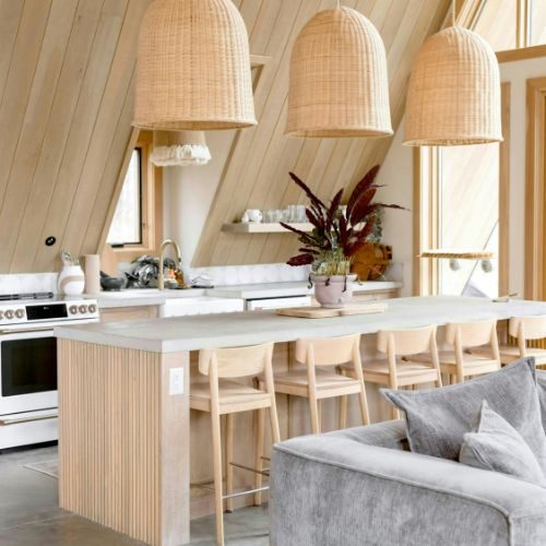 A light timber battened island with a stone benchtop under rattan pendants in an Auburn kitchen by 10X Joinery.