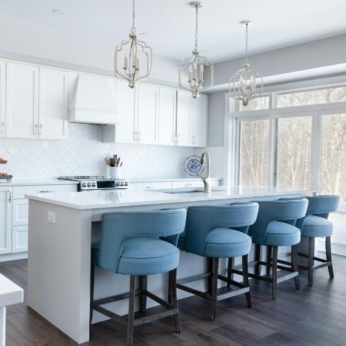A large white kitchen island with blue upholstered stools and pendant lights, sized for an Auburn family home by 10X Joinery.