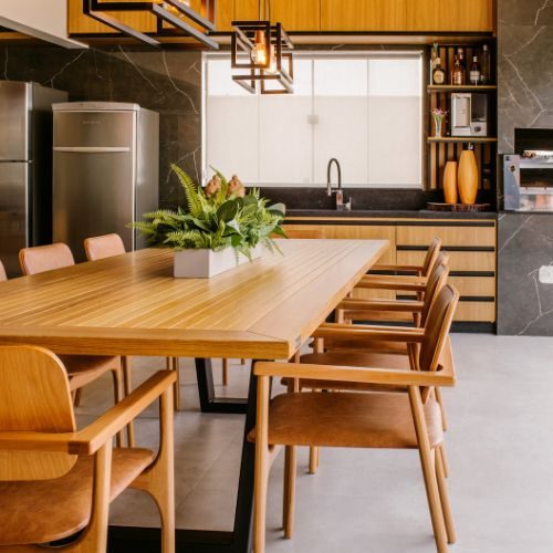 An opened-up kitchen and dining area in an established Auburn home, with timber cabinetry, a dark stone splashback and a long timber dining table by 10X Joinery.