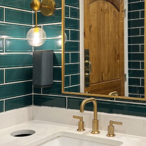 A Sydney bathroom with green subway tiles, a brass-framed mirror and brass tapware, where the joinery was coordinated with tiling and plumbing by 10X Joinery.