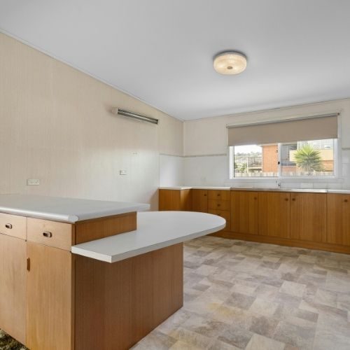 A timber kitchen with a curved white benchtop peninsula in a Baulkham Hills home, ready for new stone or laminate benchtops by 10X Joinery.
