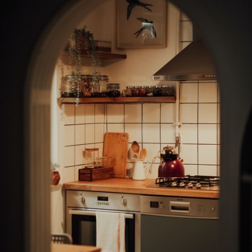 A cosy Blacktown kitchen seen through an arched doorway, with a timber-look benchtop, white square tiles and open shelving by 10X Joinery.