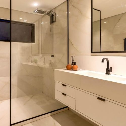 A white floating vanity with a stone benchtop beside a black-framed walk-in shower, installed by 10X Joinery.