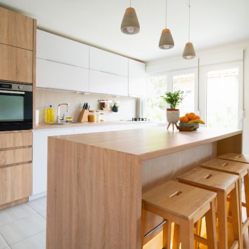 An opened-up kitchen in an established Blacktown home, with a timber island, bench seating and white overhead cabinets by 10X Joinery.
