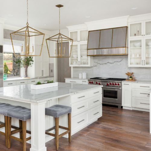 A custom kitchen design for a Bankstown home with white shaker cabinets, a marble island and brass lantern pendants by 10X Joinery.