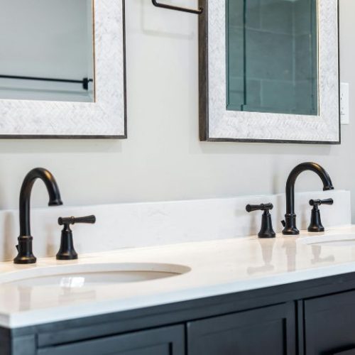 A custom navy bathroom vanity with a white benchtop, black tapware and twin mirrors, made by 10X Joinery.
