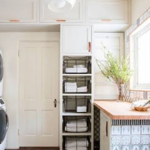 Custom white laundry and ensuite cabinetry with open basket shelving for towels, built by 10X Joinery.