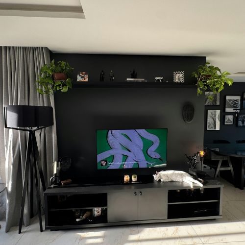 A low black entertainment unit with a floating shelf on a dark feature wall, combining TV, storage and display in a Sydney home by 10X Joinery.