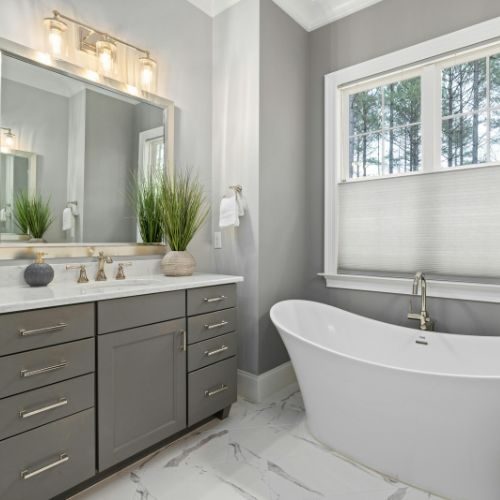 A grey shaker-style floor-standing vanity with a white benchtop beside a freestanding bath, custom built by 10X Joinery, Sydney.