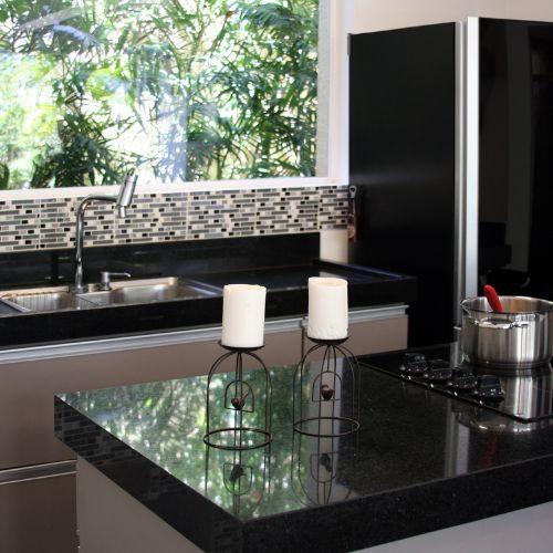 A compact granny flat kitchen in Bankstown with a black granite benchtop, mosaic splashback and gas cooktop by a garden window, built by 10X Joinery.