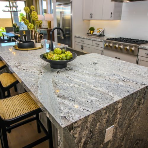 A granite waterfall kitchen island with rattan bar stools, designed for seating and storage in a Blacktown home by 10X Joinery.