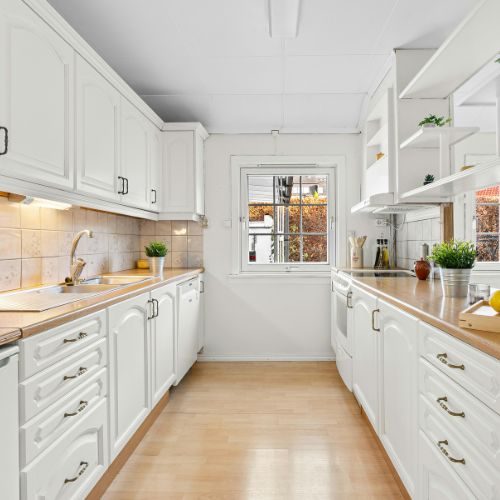 A white galley kitchen with timber benchtops, deep drawers and full-height storage in an Auburn home by 10X Joinery.