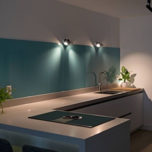 A teal glass splashback installed above a sleek cooktop and dark cabinetry in a Baulkham Hills kitchen by 10X Joinery.