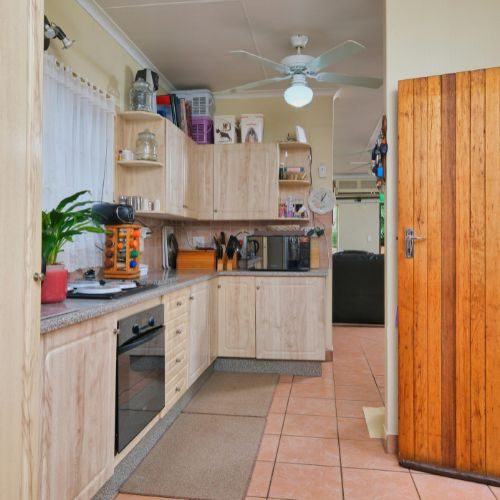 A light timber kitchen with grey benchtops and terracotta floor tiles, supplied and installed for a Blacktown home by 10X Joinery.